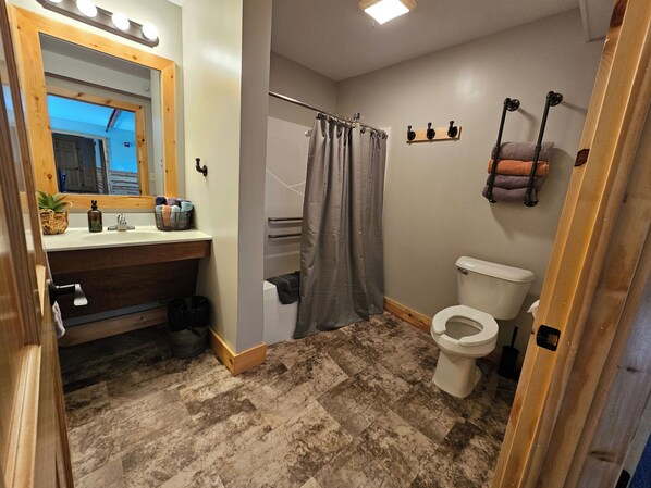 Une salle de bain avec un meuble-lavabo en bois, des toilettes, un rideau de douche et un porte-serviettes.