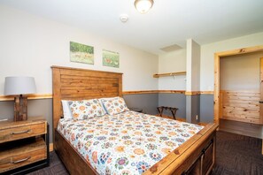 A bedroom with a wooden bed, a nightstand, a lamp, and two wall-mounted pictures.