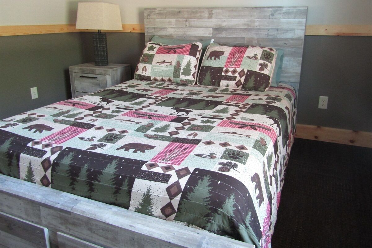 Una cama con colcha de estampados de fauna, una lámpara de noche y un cabecero de madera.