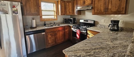 A kitchen with wooden cabinets, a stainless steel refrigerator, a microwave, a stove, and a coffee maker.