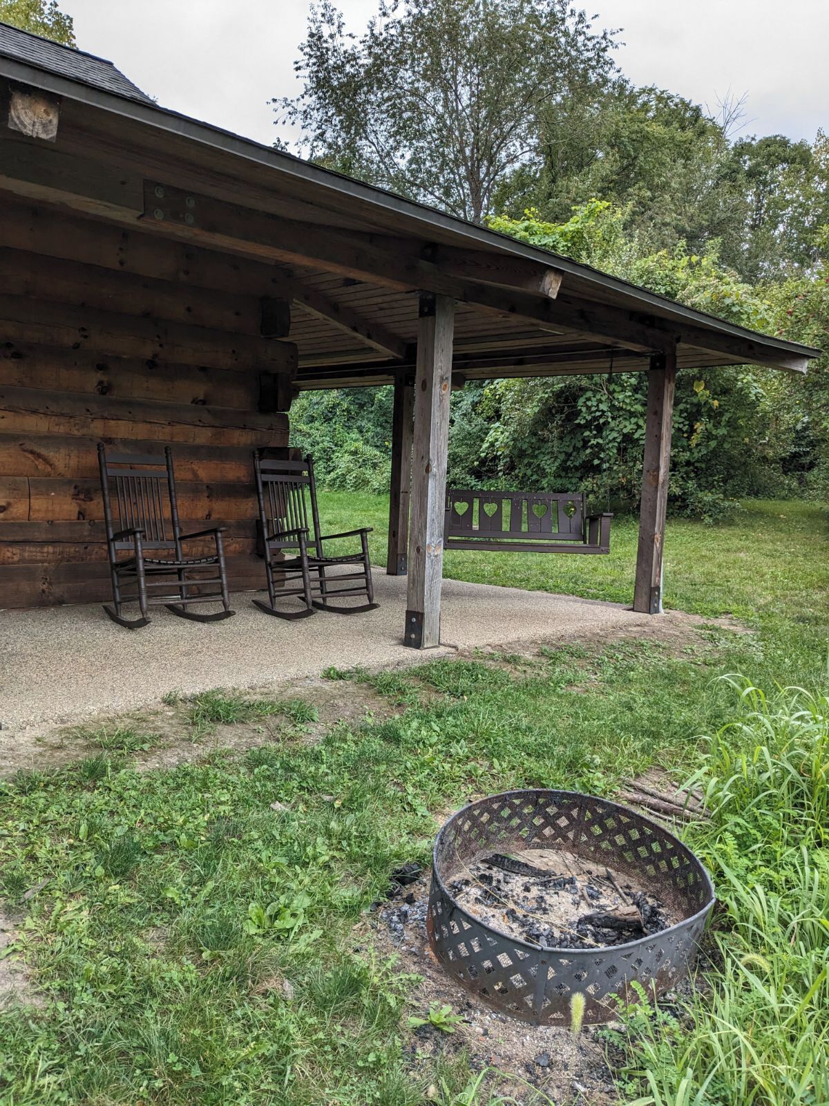 Une cabane en bois dotée d’un porche couvert, de meubles d’extérieur et d’un foyer.