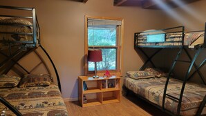 Un dormitorio con literas, una ventana, una estantería de madera con libros y una lámpara roja.