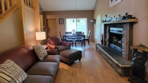 Una sala de estar con chimenea, una escalera de madera, una zona de comedor y un sofá con cojines.