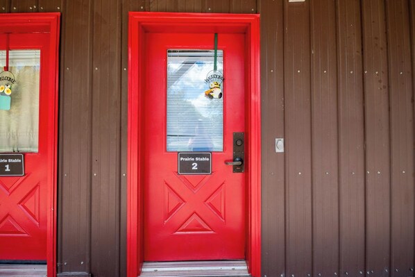 Two red doors with 'Prairie Stable' signs, numbered 1 and 2, and a welcome sign with a cartoon character.