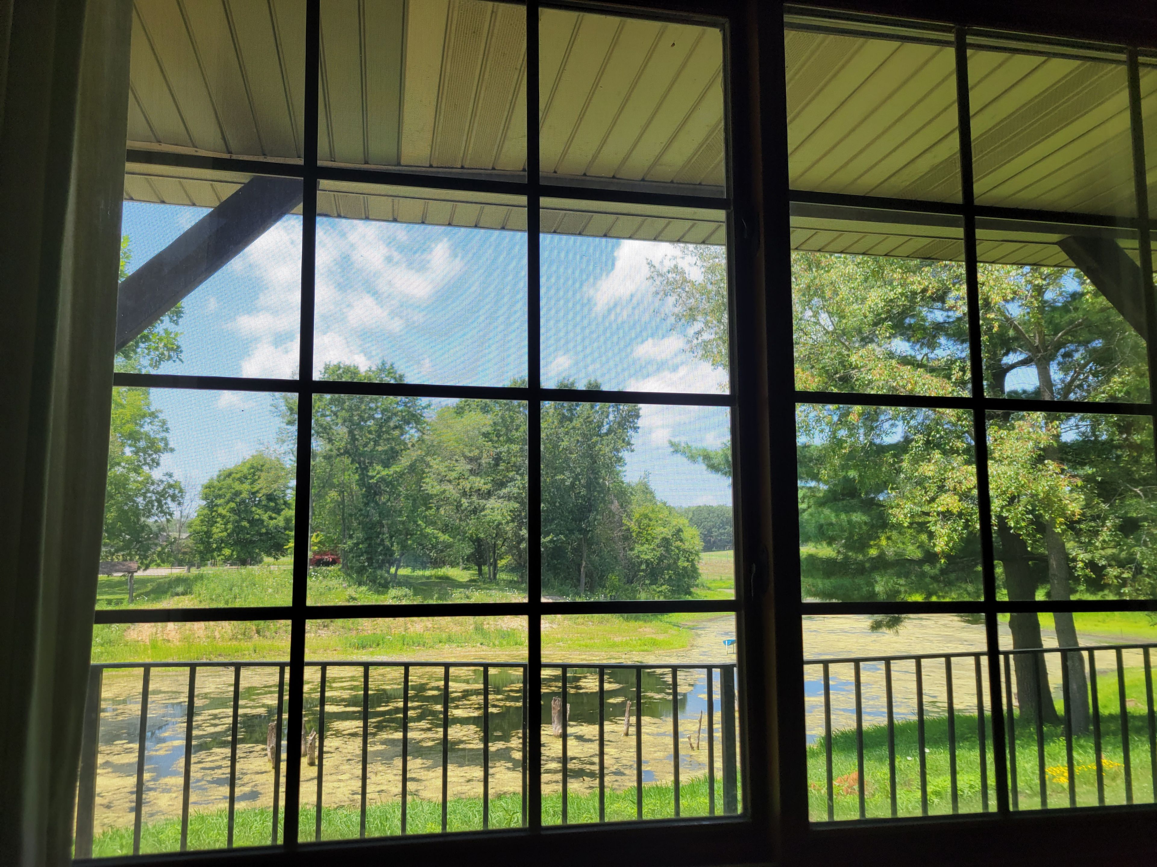 Ein Zimmer mit großem Fenster und Blick auf eine grüne Fläche mit Bäumen und einem Gewässer.