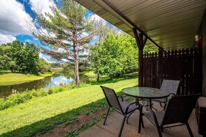 An outdoor patio with a table and chairs, overlooking a pond and trees.