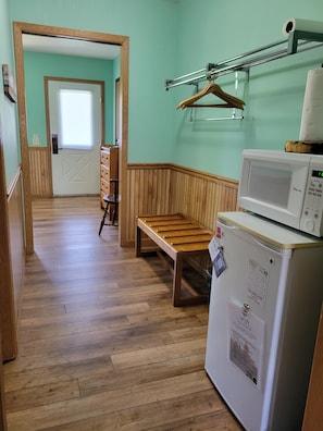 Un couloir avec un banc en bois, un four à micro-ondes et une porte donnant sur une autre pièce.