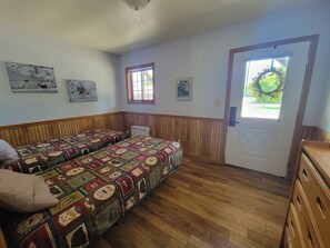 Ein Zimmer mit zwei Betten, Holzboden, einer Tür mit einem Kranz und an der Wand hängenden Bildern.