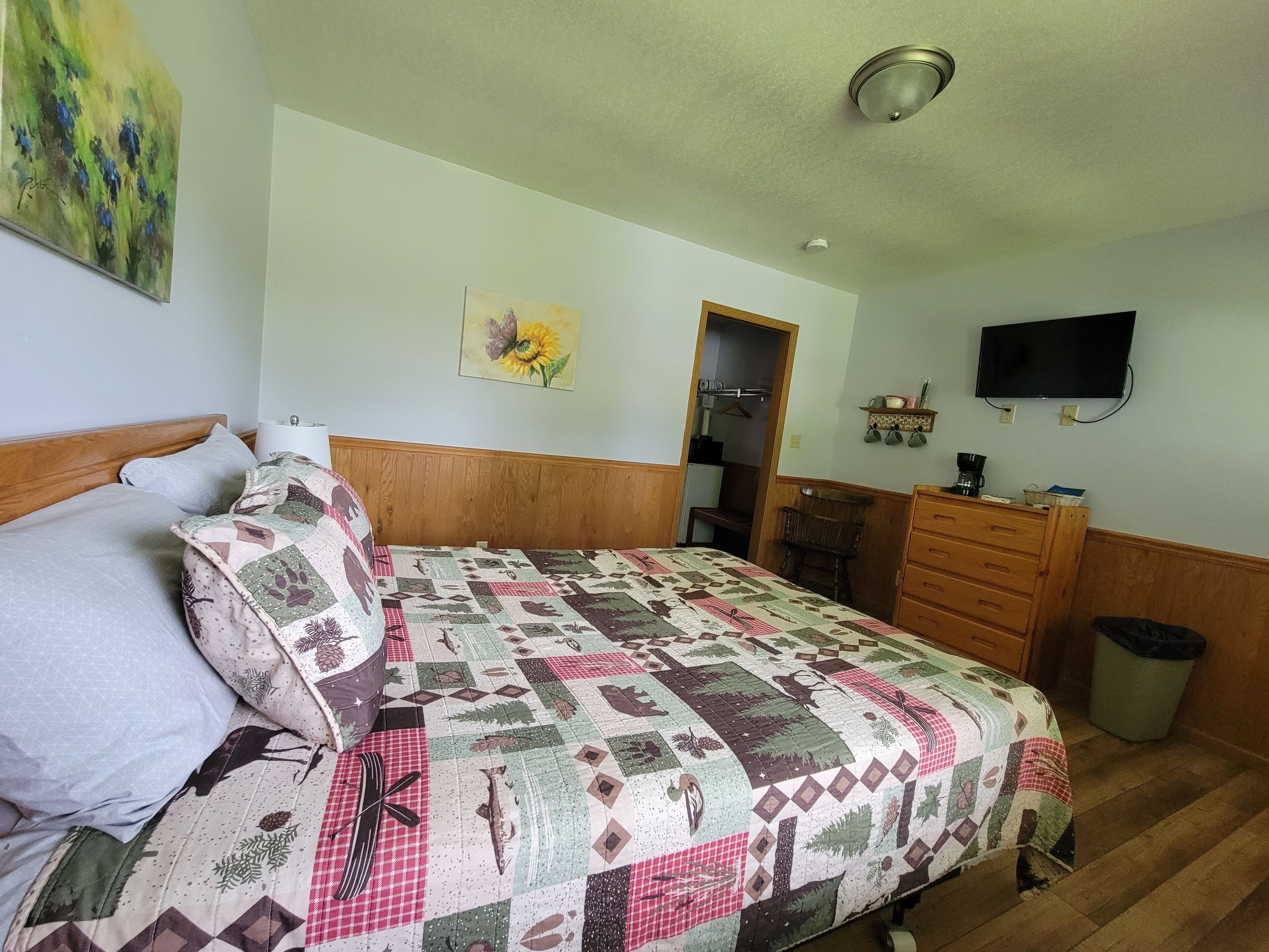 A bedroom with a bed, a dresser, a television, and a painting on the wall.