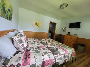 A bedroom with a bed, a dresser, a television, and a painting on the wall.