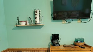 A cozy room with a wooden chair, a wooden dresser, a coffee maker, and a flat-screen TV mounted on the wall.