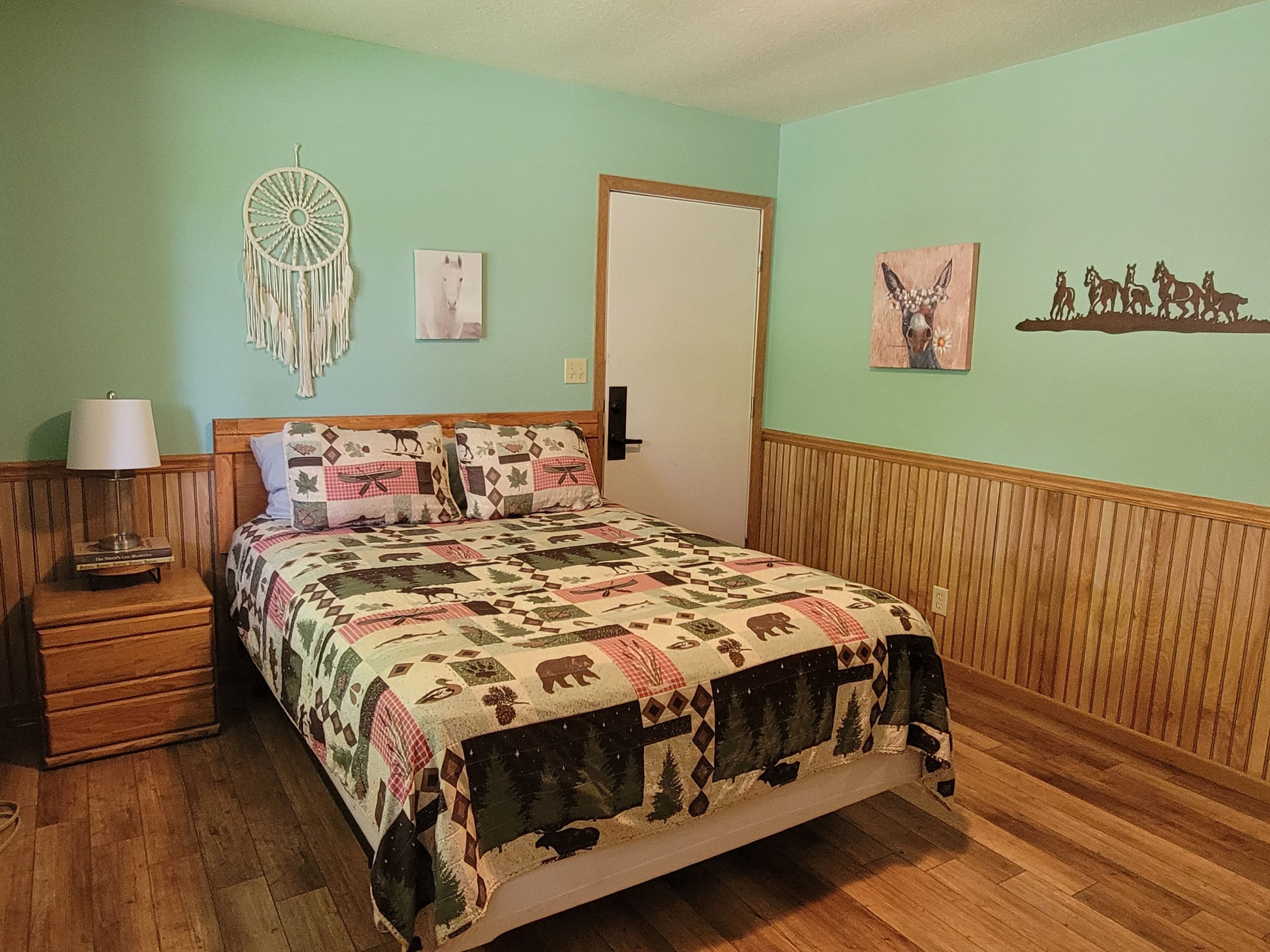 A bedroom with a bed, a nightstand, a lamp, and wall decorations including a dreamcatcher and framed pictures.