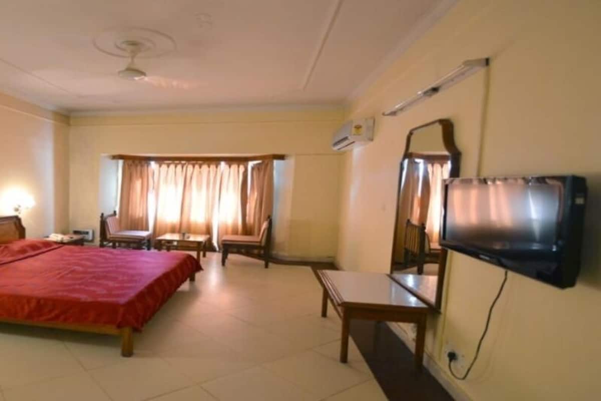 Ein Hotelzimmer mit einem großen Bett, einem Schreibtisch, einem Sessel, einem Fernseher und einem Fenster mit Vorhängen.