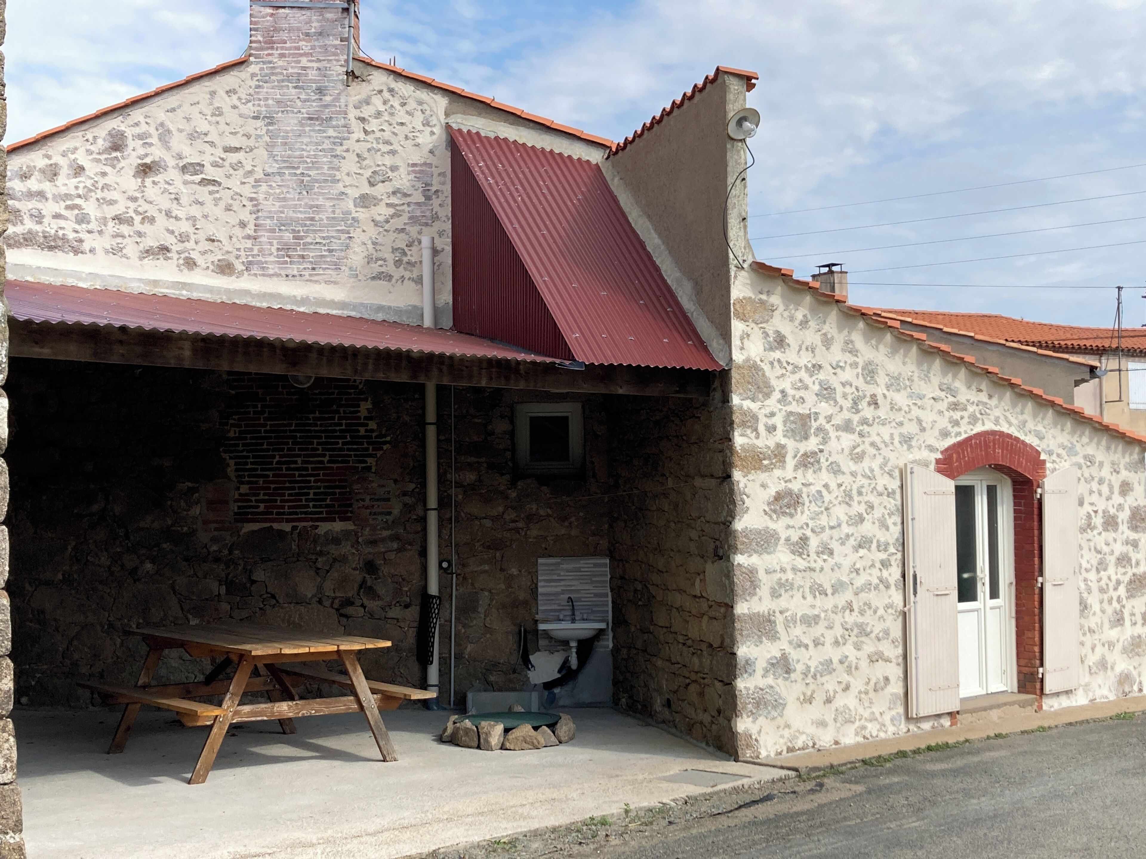 A stone building with a red roof, a wooden bench, and a door.