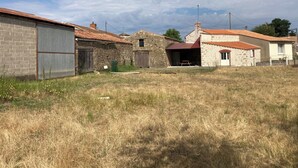 Entorno rural con edificios de piedra, una estructura de metal corrugado y un campo cubierto de hierba.