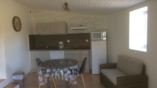Un espacio habitable compacto con zona de cocina, una mesa de comedor con sillas, un sofá y una ventana que proporciona luz natural.