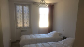 Una habitación pequeña con dos camas, una ventana con cortinas y un ventilador de techo.