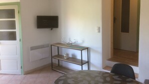 Una habitación con una televisión montada en la pared, una mesita con una taza y una silla.