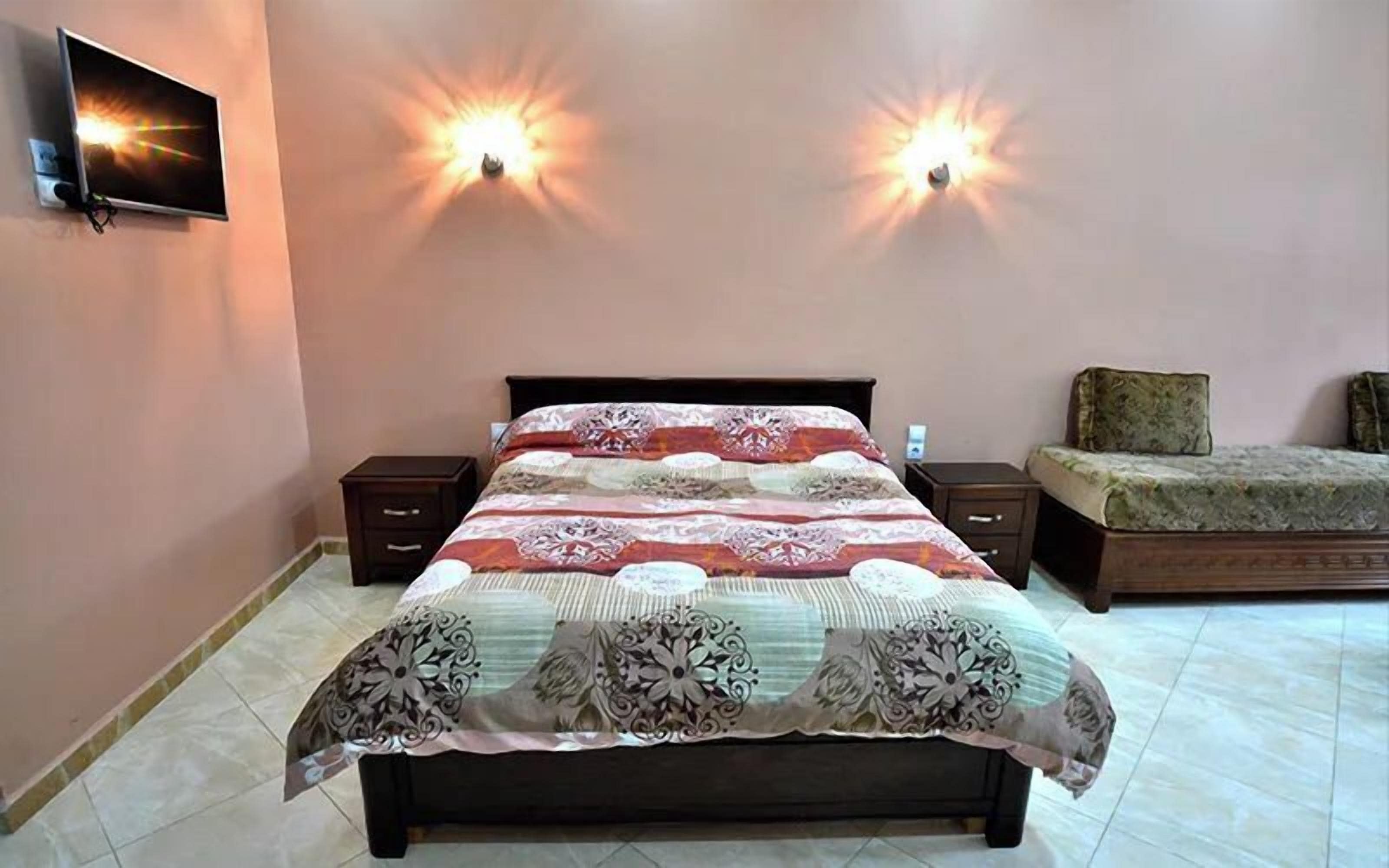 Un dormitorio con una cama, dos mesitas de noche y dos lámparas de pared.