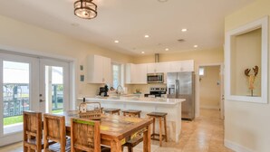 A spacious kitchen with white cabinets, a central island, and a dining area with wooden chairs and a table. - Castaway Cottage (St. Augustine)
