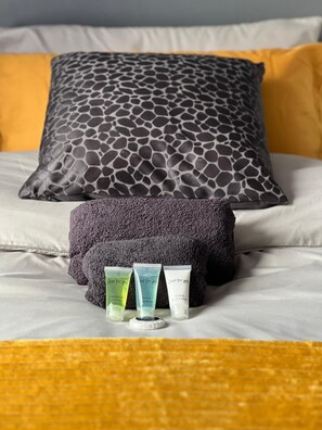 A bed with two pillows, one with a giraffe pattern and another plain. There are three toiletries on the bed.