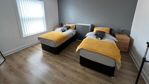 A bedroom with two beds, a window with blinds, a bedside table with a lamp, and a wardrobe. - City Escape - Charming 2-bed House (Leeds)