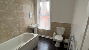 A bathroom with a bathtub, sink, toilet, and a window with blinds. - City Escape - Charming 2-bed House (Leeds)