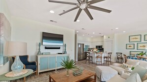 A spacious living room with a ceiling fan, a television, and a kitchen in the background. - Endless Sea (Santa Rosa Beach)