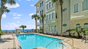 A pool area with a view of the ocean, surrounded by palm trees and a building with multiple balconies. - Endless Sea (Santa Rosa Beach)