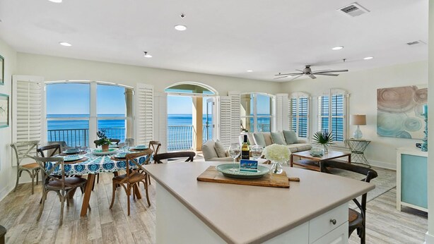 A spacious dining area with a large table, chairs, and a view of the ocean through open windows. - Endless Sea (Santa Rosa Beach)