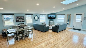 A spacious living room with a wooden floor, a dining area with a table and chairs, a gray sofa, and a television mounted on the wall. - Top Mast Resort-Anchor House, Private Beach Access. (North Truro)