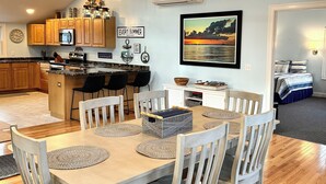 A modern kitchen with wooden cabinets, a central island, and a dining area with a table set for four. - Top Mast Resort-Anchor House, Private Beach Access. (North Truro)