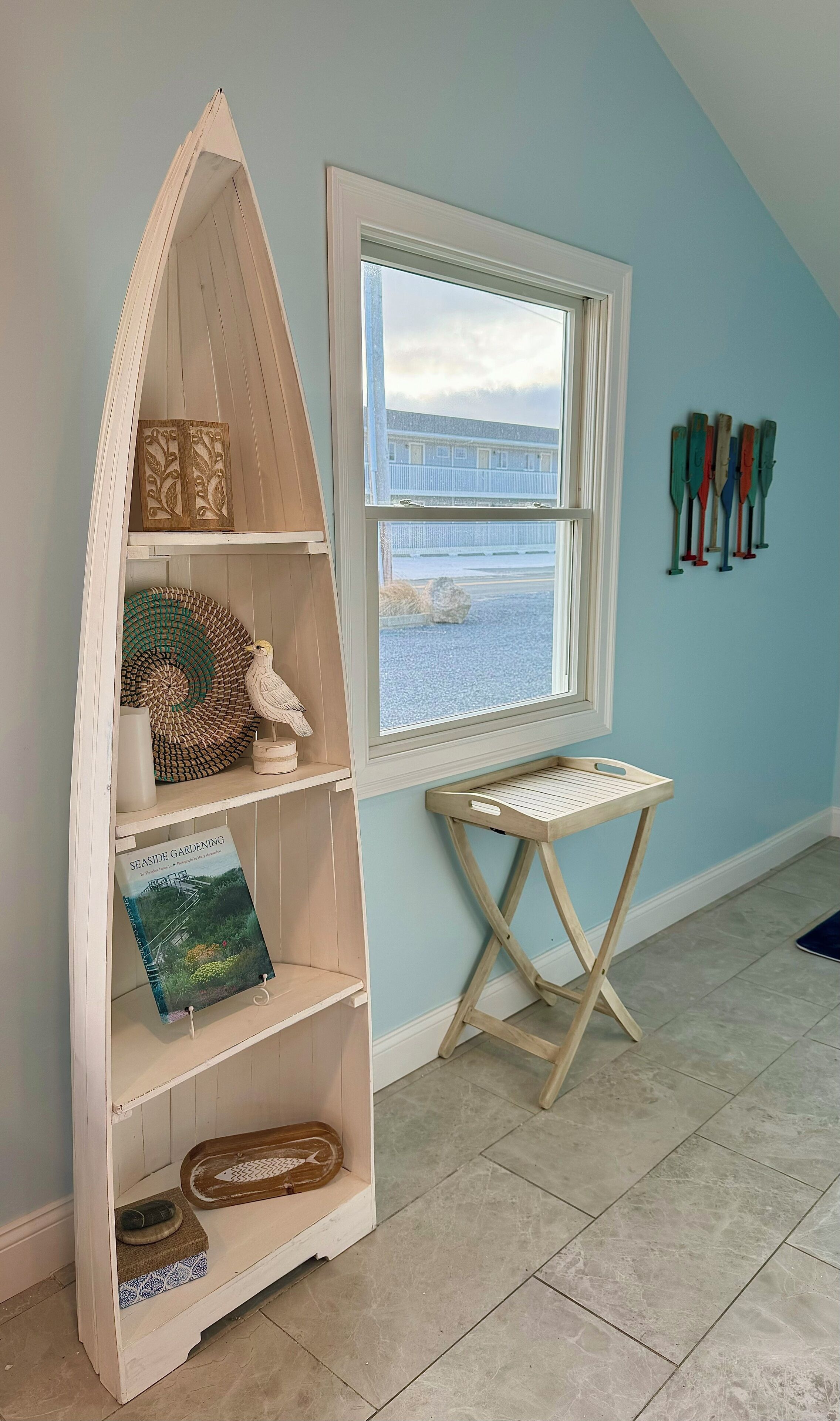 A room with a wooden bookshelf, a small table, and a window with a view of a building and a body of water.