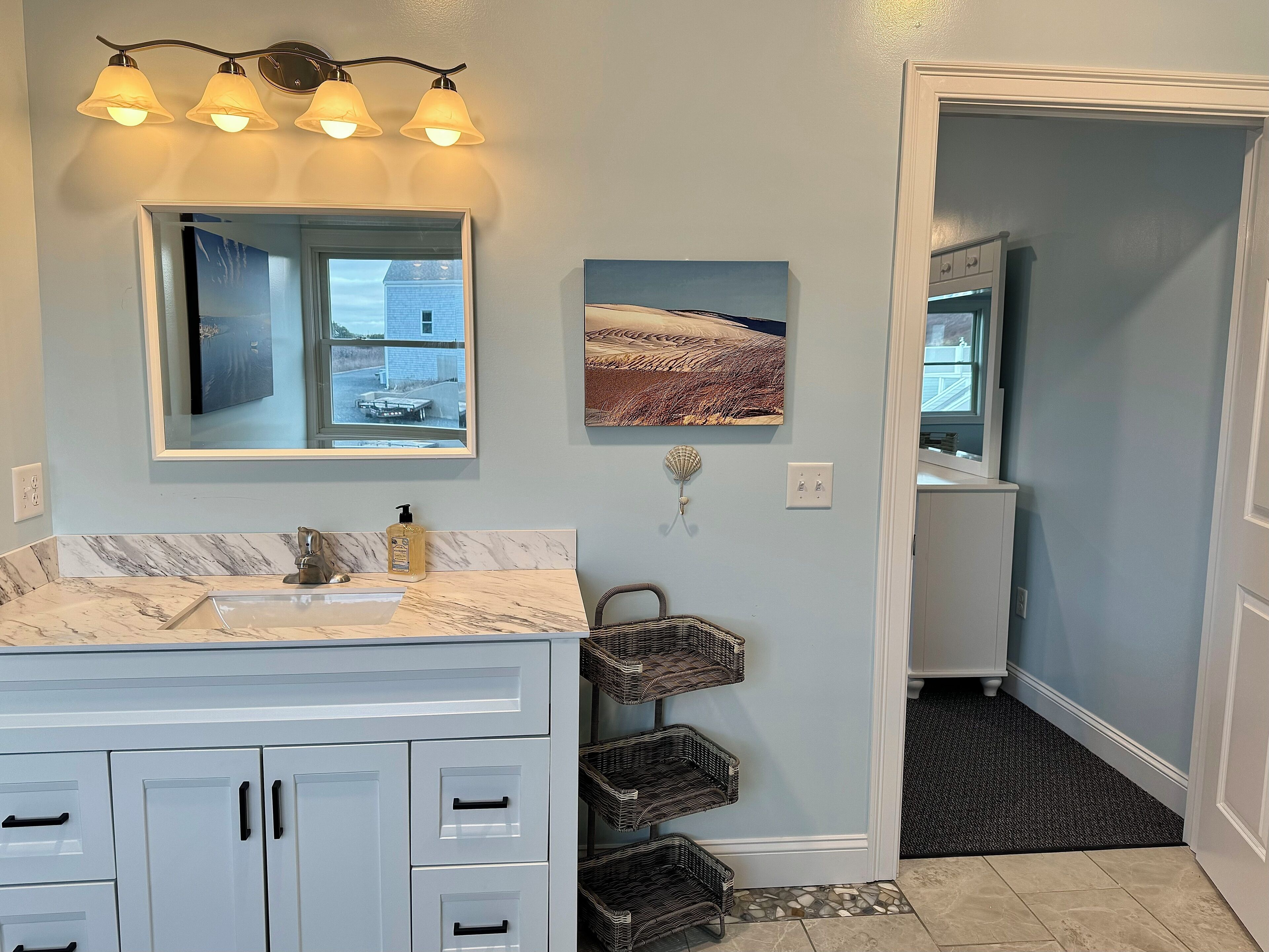 A bathroom with a marble sink, white cabinets, a mirror, and wall-mounted lights. There are two framed pictures on the wall.
