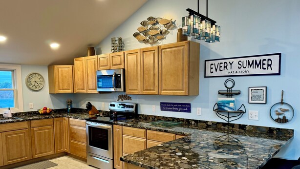 A modern kitchen with wooden cabinets, granite countertops, stainless steel appliances, and decorative wall art. - Top Mast Resort-Anchor House, Private Beach Access. (North Truro)