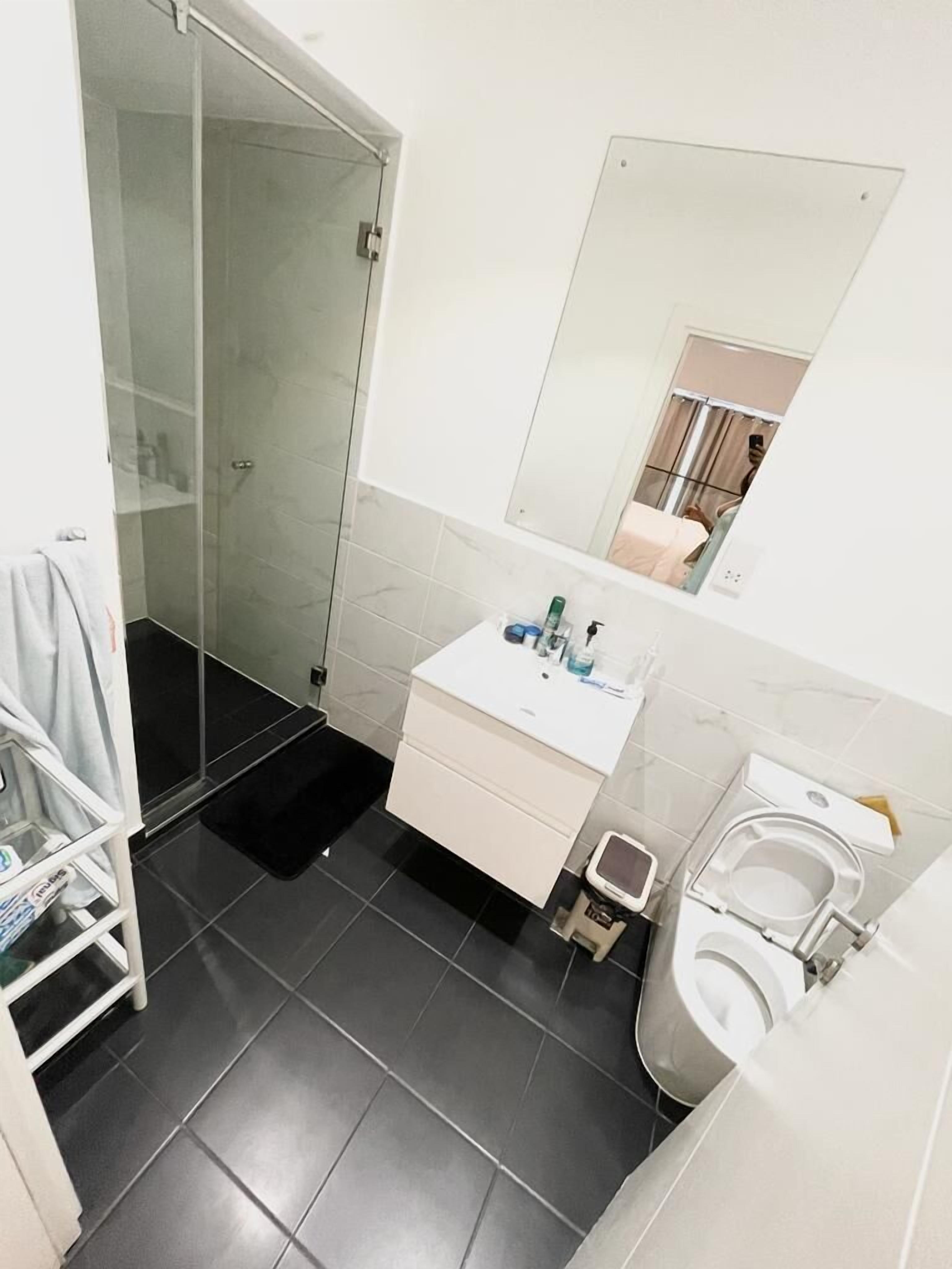 A bathroom with a glass shower enclosure, a white sink with toiletries, and a toilet.