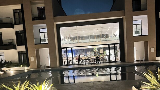 A modern building with a large glass entrance, outdoor seating area, and a reflective pool.