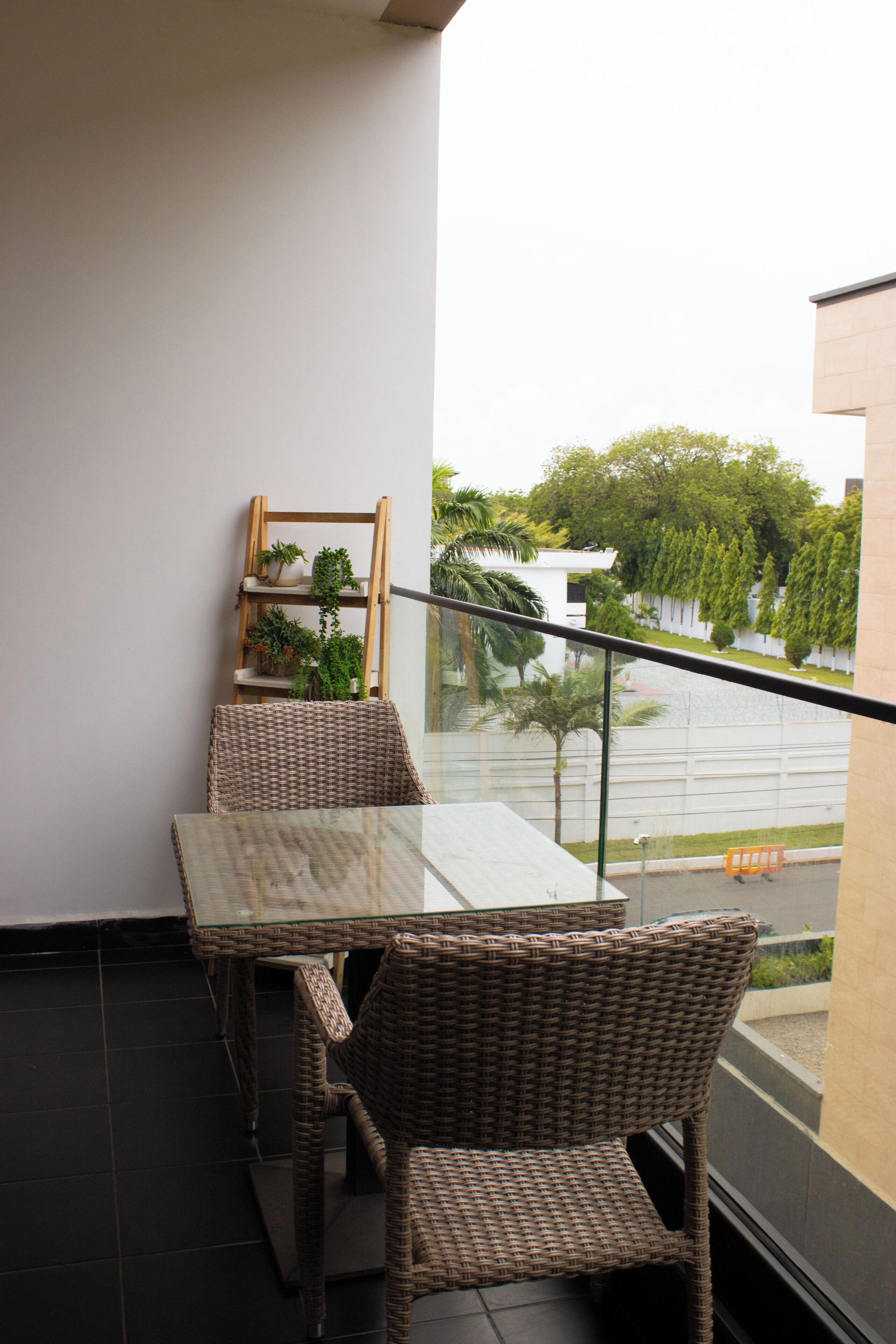 A balcony with wicker furniture, a glass table, and potted plants.