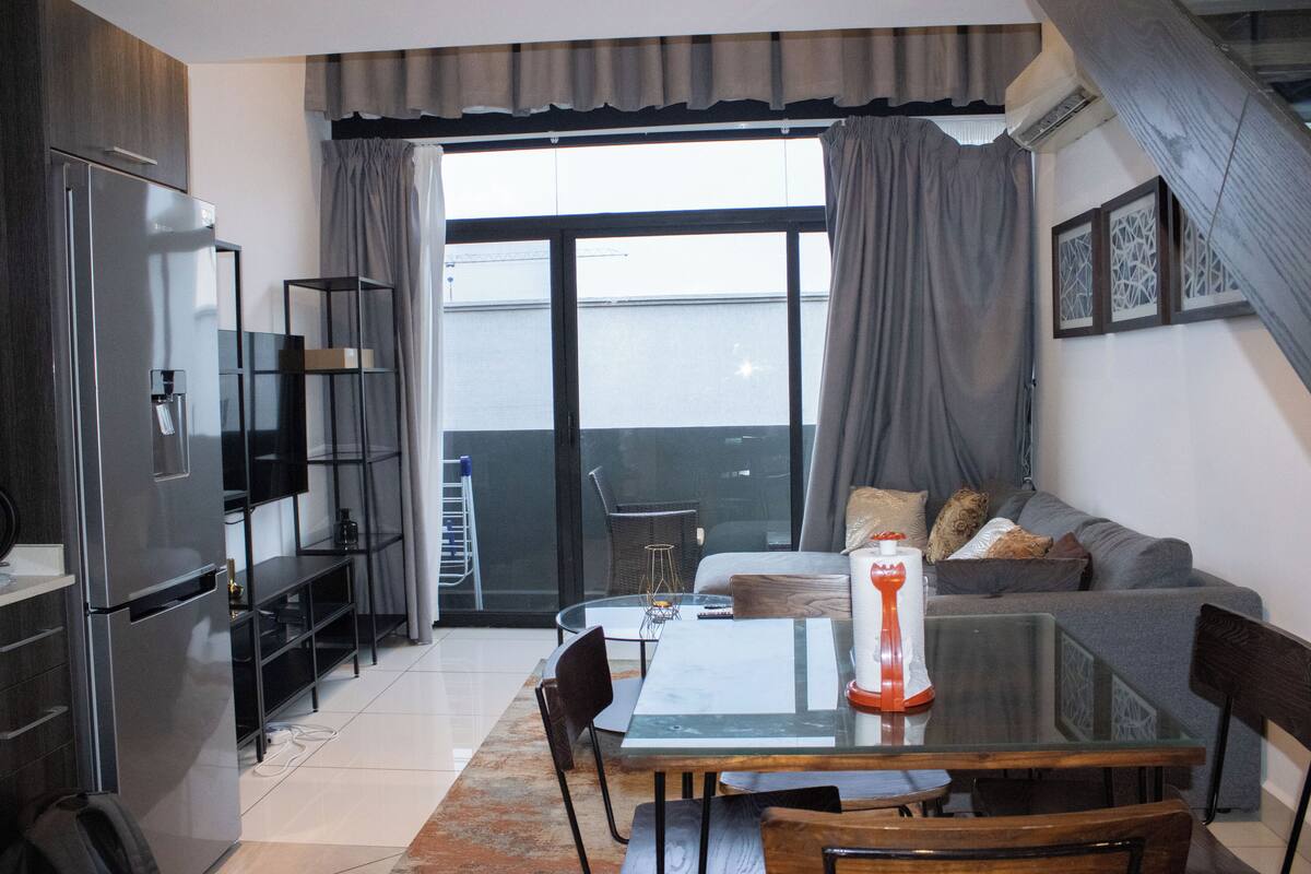 Een moderne keuken met een koelkast, een eettafel en stoelen. Er is een balkon met uitzicht op de stad.