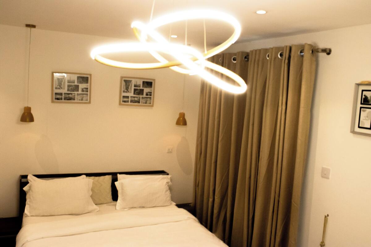 Een hotelkamer met een bed, een modern lamparmatuur en twee ingelijste foto's aan de muur.