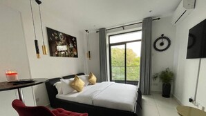 A modern bedroom with a large bed, a desk, a red chair, and a potted plant.