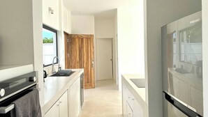Eine moderne Küche mit Backofen, Spüle und Kühlschrank. Eine Holztür führt in einen anderen Raum.
