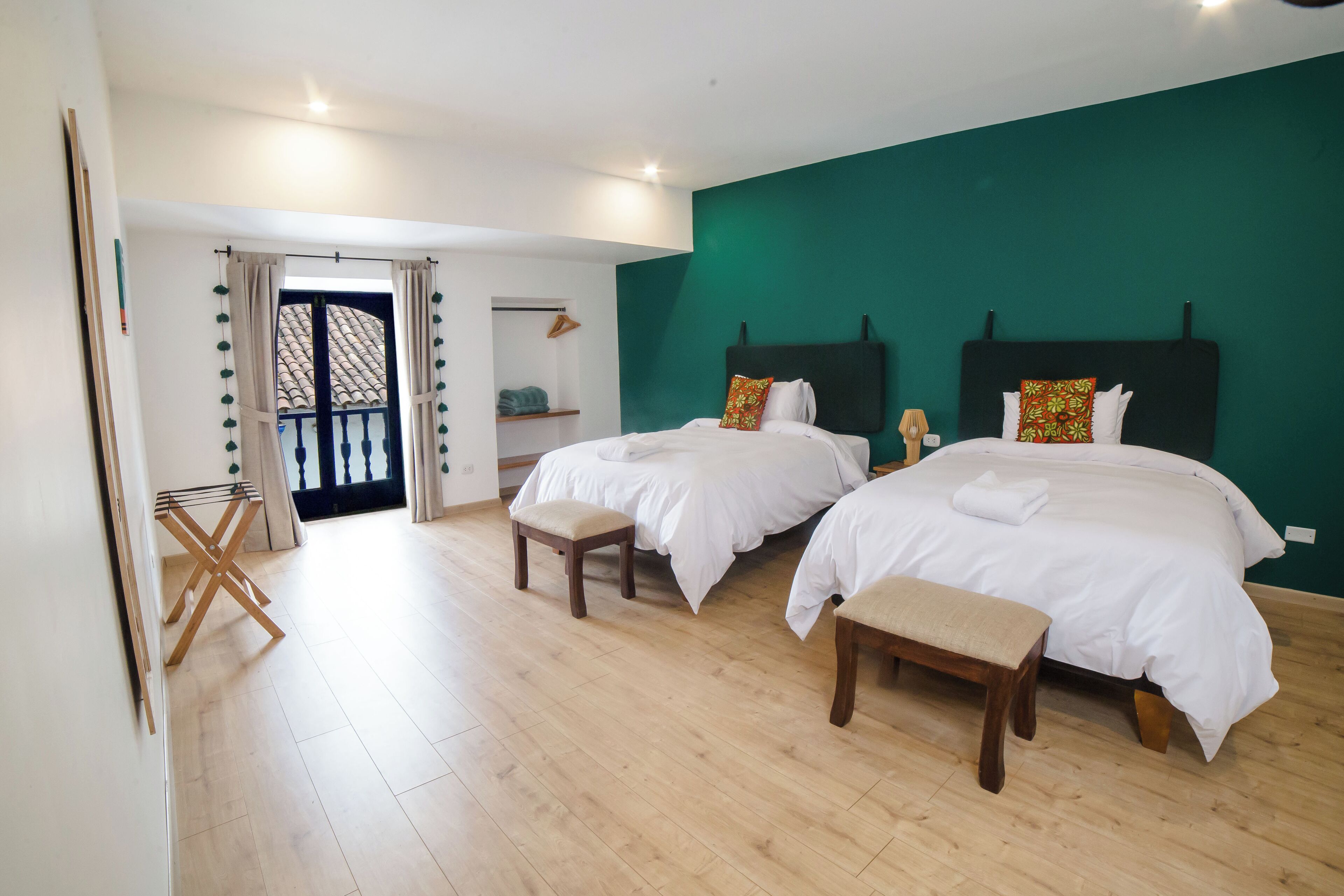 A hotel room with two beds, a wooden floor, a green accent wall, and a balcony with a view.