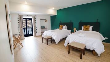 A hotel room with two beds, a wooden floor, a green accent wall, and a balcony with a view.
