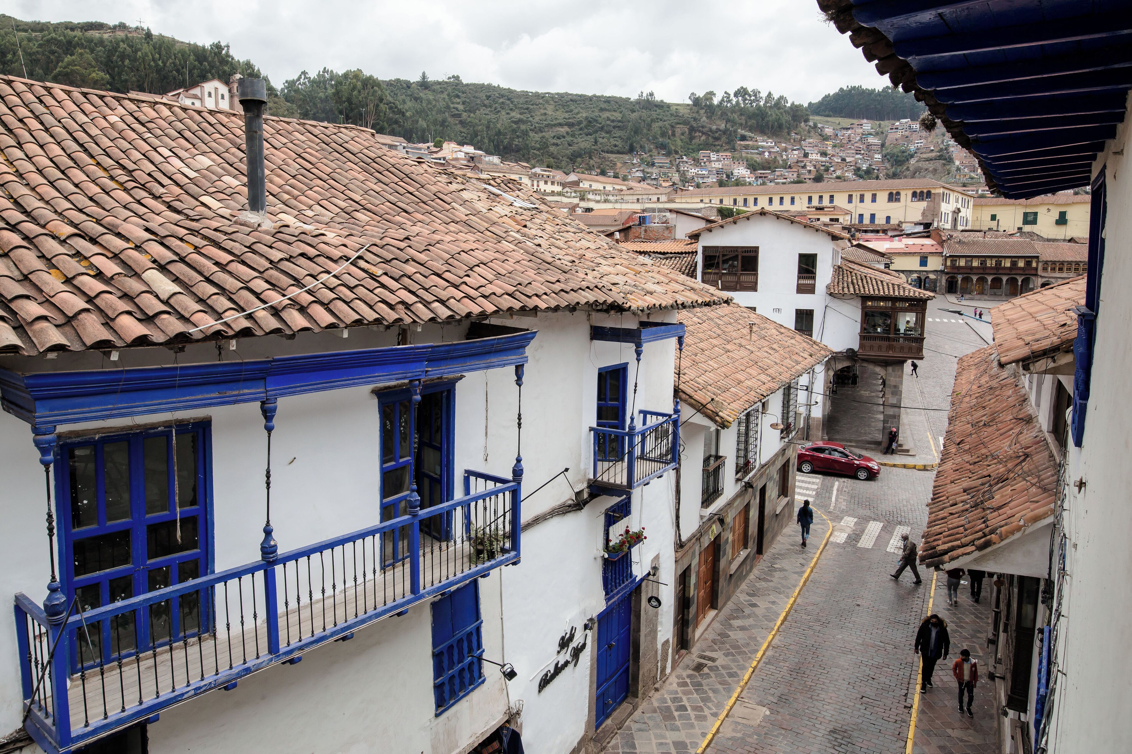 A narrow street with traditional buildings, a red car, and pedestrians.