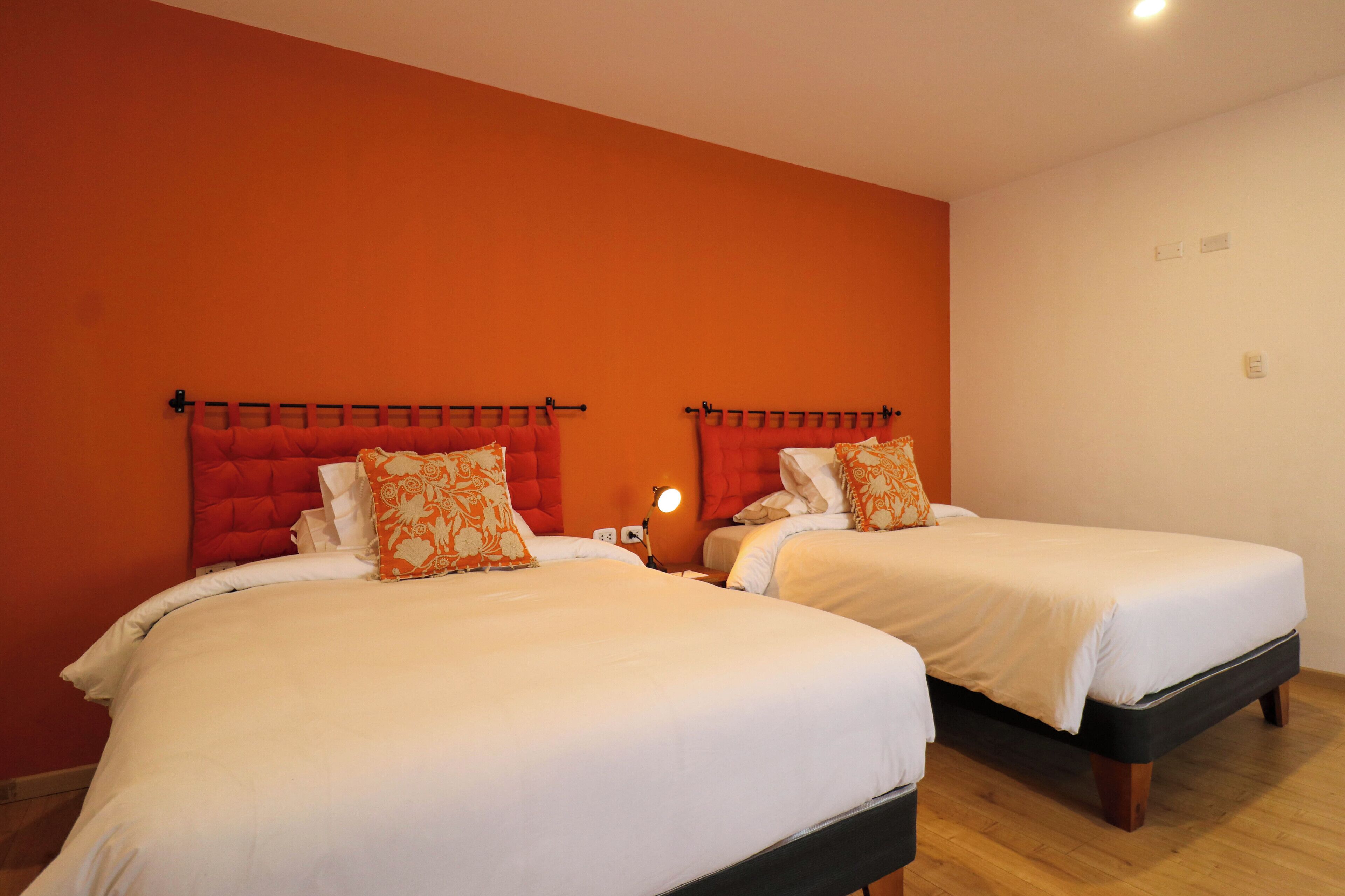 Two single beds with red headboards in a room with orange walls and wooden flooring.