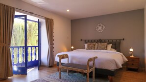 Un dormitorio con cama, una silla de madera, una mesita de noche y un ventanal con cortinas.