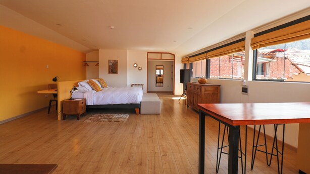 Un dormitorio con cama, mesitas de noche, escritorio y ventana con cortinas.