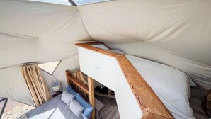 Un hébergement sous tente comprenant un lit superposé, une petite table et une lampe.