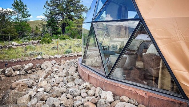 Une tente en forme de dôme géodésique offrant une vue dégagée sur l’intérieur, notamment sur le lit et la fenêtre.